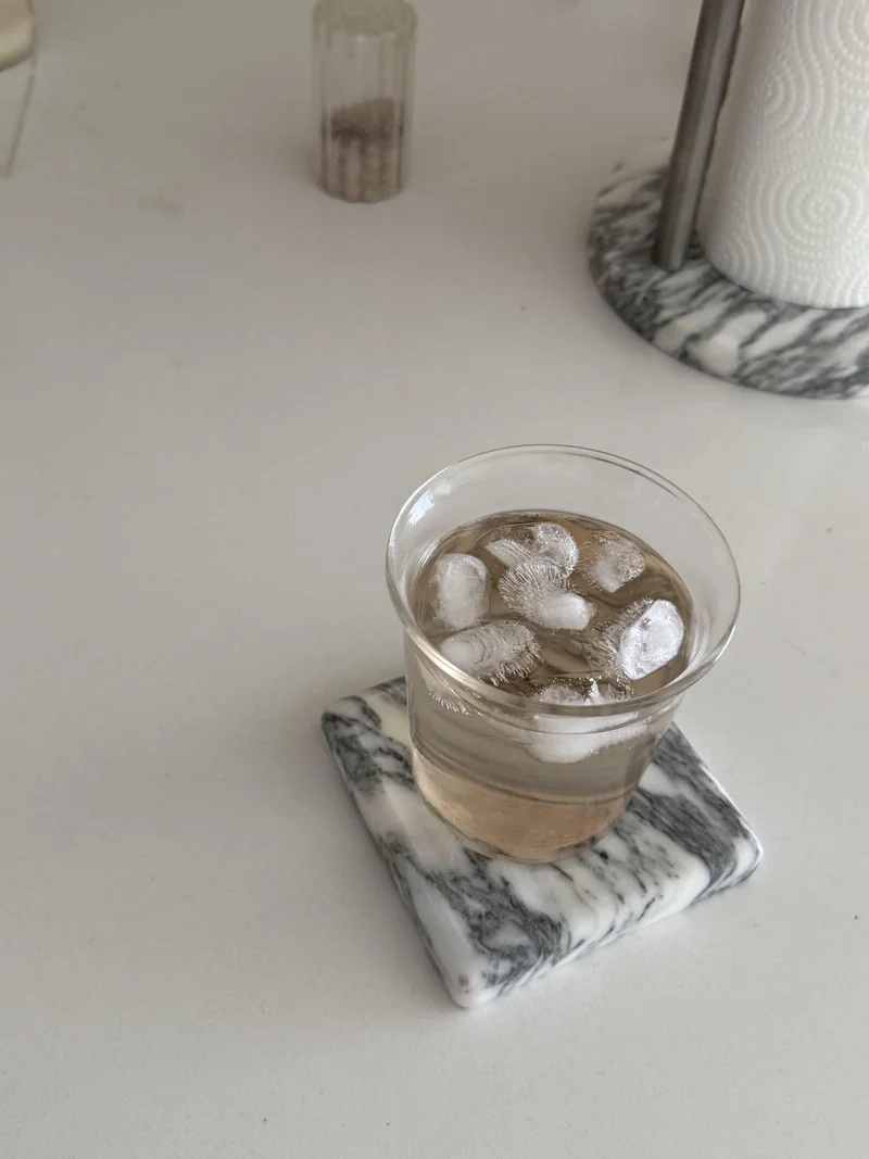 Glass of iced drink resting on a pale stone coaster with dark veins