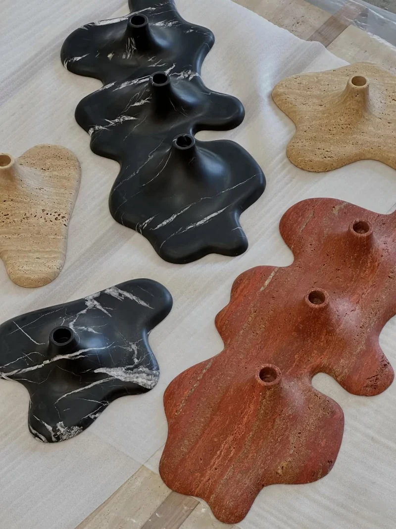 Organic-shaped black, beige and red stone candleholder bases arranged on a workshop surface