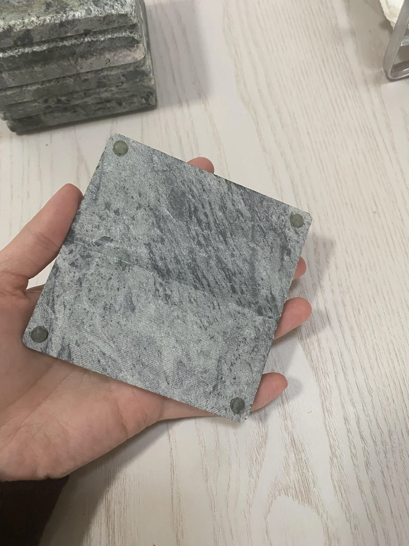 Underside of a grey stone coaster held in a hand, with four round feet visible