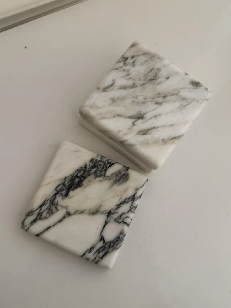 Stack of pale square stone coasters with dark veins and rounded corners