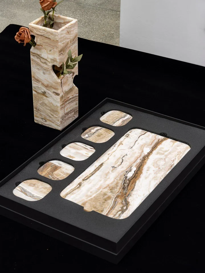 Banded stone rectangular tray and five small rounded pieces in fitted foam beside a tall decorative vessel