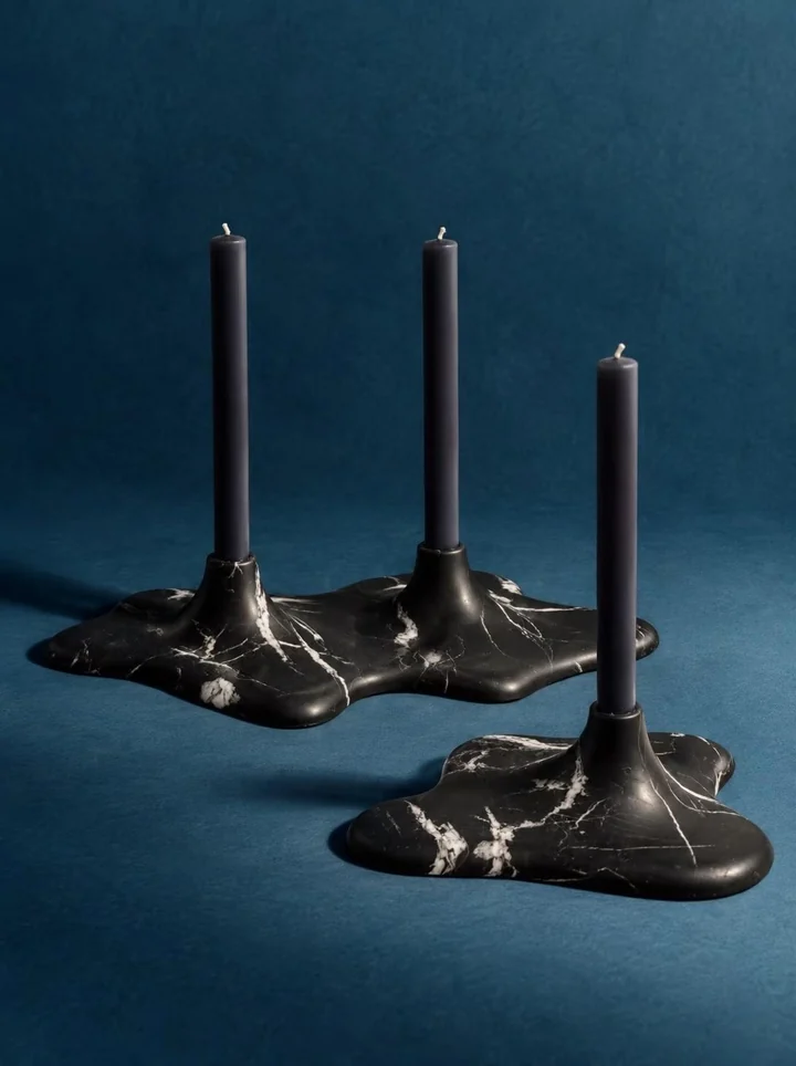 Three black veined stone candleholders with flowing bases and unlit taper candles against a blue background