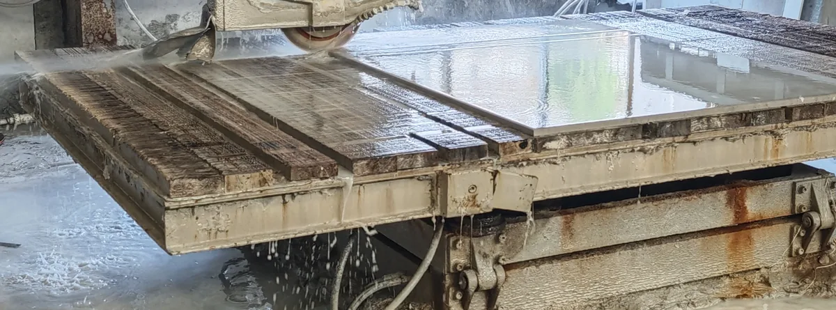 Water-cooled saw blade cutting a stone panel on the workshop cutting bed