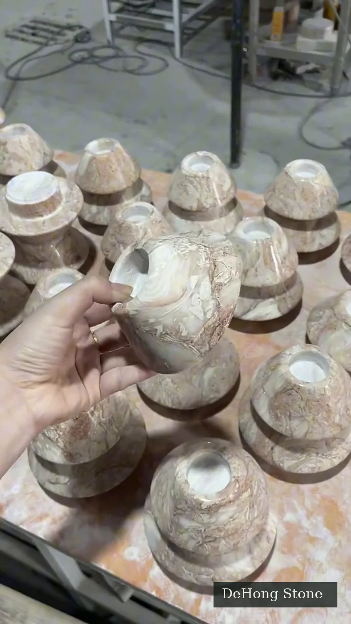 Hand holding a small shaped stone piece beside other stone objects in the DeHong Stone workshop
